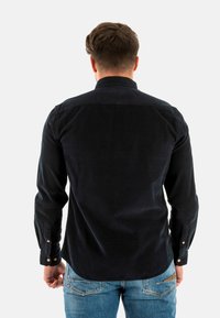Chemise boutonnée bleu marine foncé en tissu texturé, avec un col classique et des poignets à boutons, associée à un jean en denim bleu clair.
