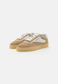 Brune semskede sneakers med hvite lærdetaljer, teksturert overflate, flate snørebånd og såle i gummigummi, med perforeringer på siden for pusteevne.