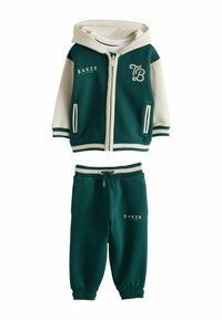 Sudadera con cremallera en verde y crema con acentos de logo y dos bolsillos laterales, combinada con pantalones de chándal verdes a juego que cuentan con un cordón y logo.