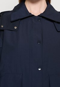Mørkeblå skjortejakke med stor krave, der har to brystlommer og trykknaplukninger. Materialet virker glat og let.