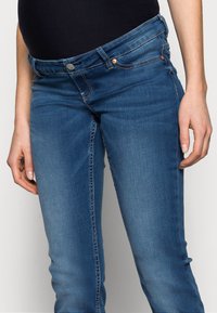 Jeans de ganga em azul médio, com um corte clássico afunilado, cintura de altura média e detalhes em prata com costura em contraste.
