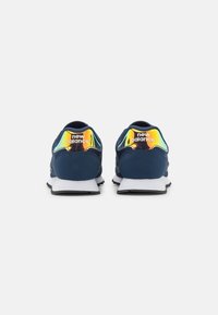 Pair of navy blue New Balance sneakers shown from the back, featuring reflective rainbow heel tabs and white midsoles on a white background.