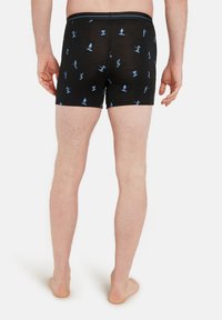 Bakifrån av en man som bär svarta boxershorts med ljusblå mönster av skidåkning och snowboard.