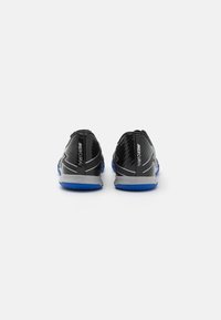 Zwarte voetbalschoenen met een glanzende afwerking, voorzien van een blauwe rubberen zool en zilveren accenten. Het achteraanzicht toont de branding en gestructureerde details.