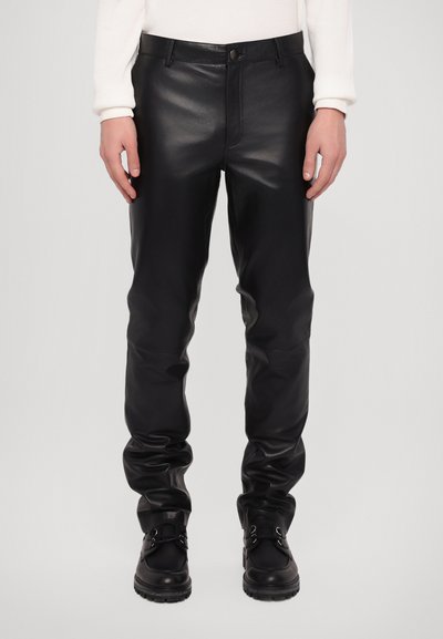 Zwarte leren broeken met een aansluitend ontwerp, voorzien van een knoopsluiting en een gladde textuur. Gecombineerd met zwarte laarzen, wat de look compleet maakt.