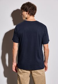 Marinblå kortärmad T-shirt i bomull, med rund halsringning och enkel design. Bärs med ljusbeige byxor.