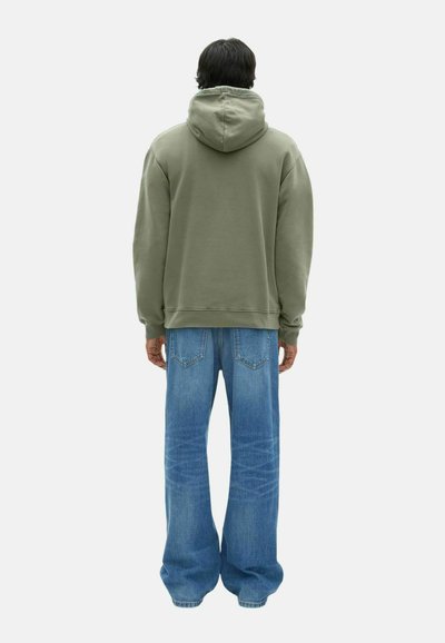 Haut à capuche oversized vert olive avec un cordon de serrage, associé à un jean bleu à jambes larges avec des poches arrière et un délavage clair.
