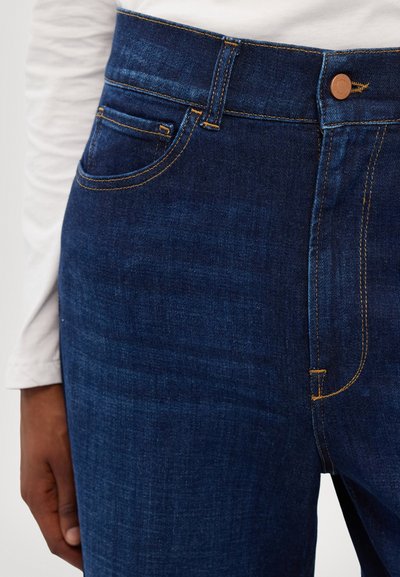 Jeans de mezclilla azul oscuro con costuras visibles, un bolsillo frontal y cierre de botón. El material tiene una textura suave y un acabado ligeramente deslavado.