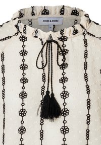 Cremefarbene Bluse mit schwarzer Blumenstickerei und Quastenakzenten. Verfügt über einen gerafften Ausschnitt und einen strukturierten Stoff mit kleinen erhabenen Punkten.