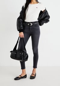 Chaqueta bomber acolchada negra, camiseta ajustada blanca, cinturón negro con tachuelas, jeans skinny de mezclilla oscura, bailarinas negras con tachuelas y un bolso negro con cremalleras.