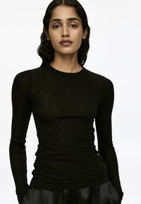 Schwarzes Langarmshirt aus leichtem, transparentem Material; figurschnitt mit rundem Ausschnitt und minimalen Nähten.