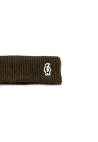 Gehaakte hoofdband in donkergroen, met een geribbelde textuur en een wit pinguïnlogo patch. Eenvoudig, veelzijdig ontwerp voor warmte.