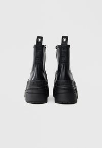 Svarte platåstøvler med glatt skinnoverdel, glidelåslukking, forsterket hæl og preget "BUFFALO"-merke på siden.