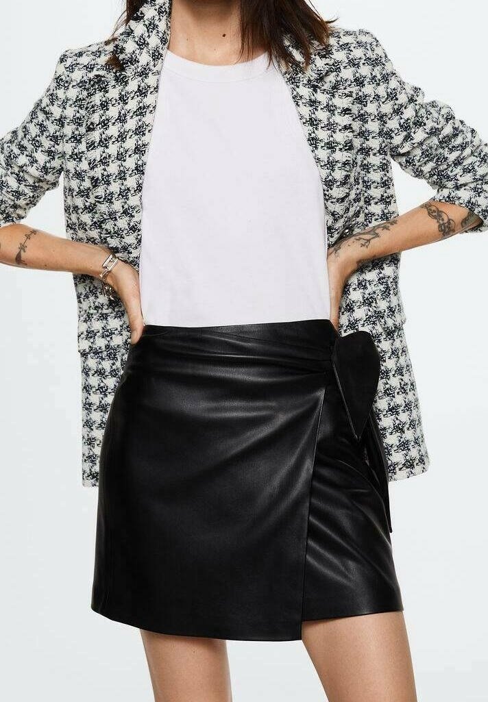 Jupe enveloppante en cuir noir avec un lien sur le côté, associée à un t-shirt blanc et un blazer en tweed à motif noir et blanc. Texture lisse, coupe droite.