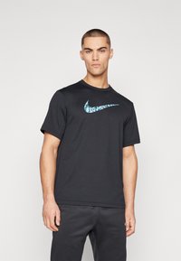 Svart treningst-skjorte laget av lett stoff, med en turkise Nike swoosh-logo i midten. Korte ermer og rund hals.