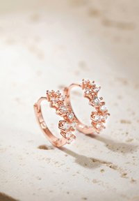 Pendientes de aro en oro rosa con una fila de pequeños cristales transparentes a lo largo del borde superior. Superficie lisa, detalle de diseño intrincado en los acentos.