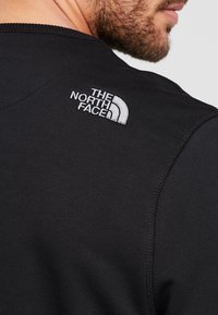 Černé sportovní tričko s hladkou texturou, na horní části zad s bílým vyšitým logem "The North Face". Viditelné švy.