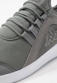 Nærbillede af grå sneakers med stofoverdel, snoede snørebånd, suedepanel på siden og hvid sål på en hvid baggrund.