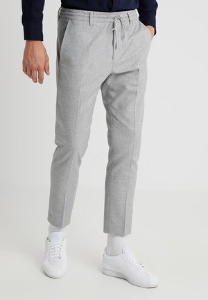 Grijze tapered broek met een elastische trekkoord taille, voorplooien en zijzakken, gecombineerd met witte sneakers.