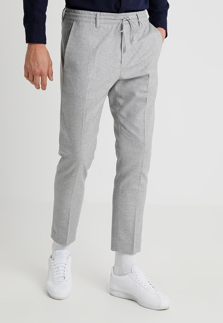 Šedé zúžené kalhoty s elastickým stahovacím pasem, předními sklady a bočními kapsami, doplněné bílými teniskami.