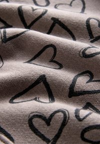 Tejido beige con un patrón repetido de formas de corazón negras, con una apariencia texturada que muestra pliegues y caídas.