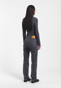 Jeans di denim grigio con una vestibilità leggermente ampia, dotati di tasche posteriori e una fettuccia in pelle marrone sul punto vita. Maglietta a maniche lunghe in cotone a coste di colore grigio scuro.