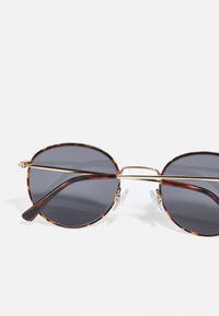Gafas de sol carey con lentes grises, puente delgado dorado y patillas marrones. Almohadillas nasales transparentes que mejoran la comodidad y el ajuste.
