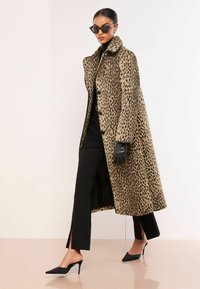 Płaszcz w panterkę z wysokim kołnierzem, z czarnymi guzikami. Noszony na czarnym stroju, w zestawieniu z czarnymi rękawiczkami i spiczastymi obcasami.