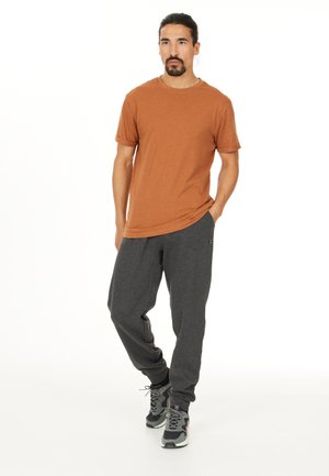 Orange short-sleeve t-shirt paired with dark gray sweatpants and gray sneakers. The fabric appears soft with a relaxed fit.