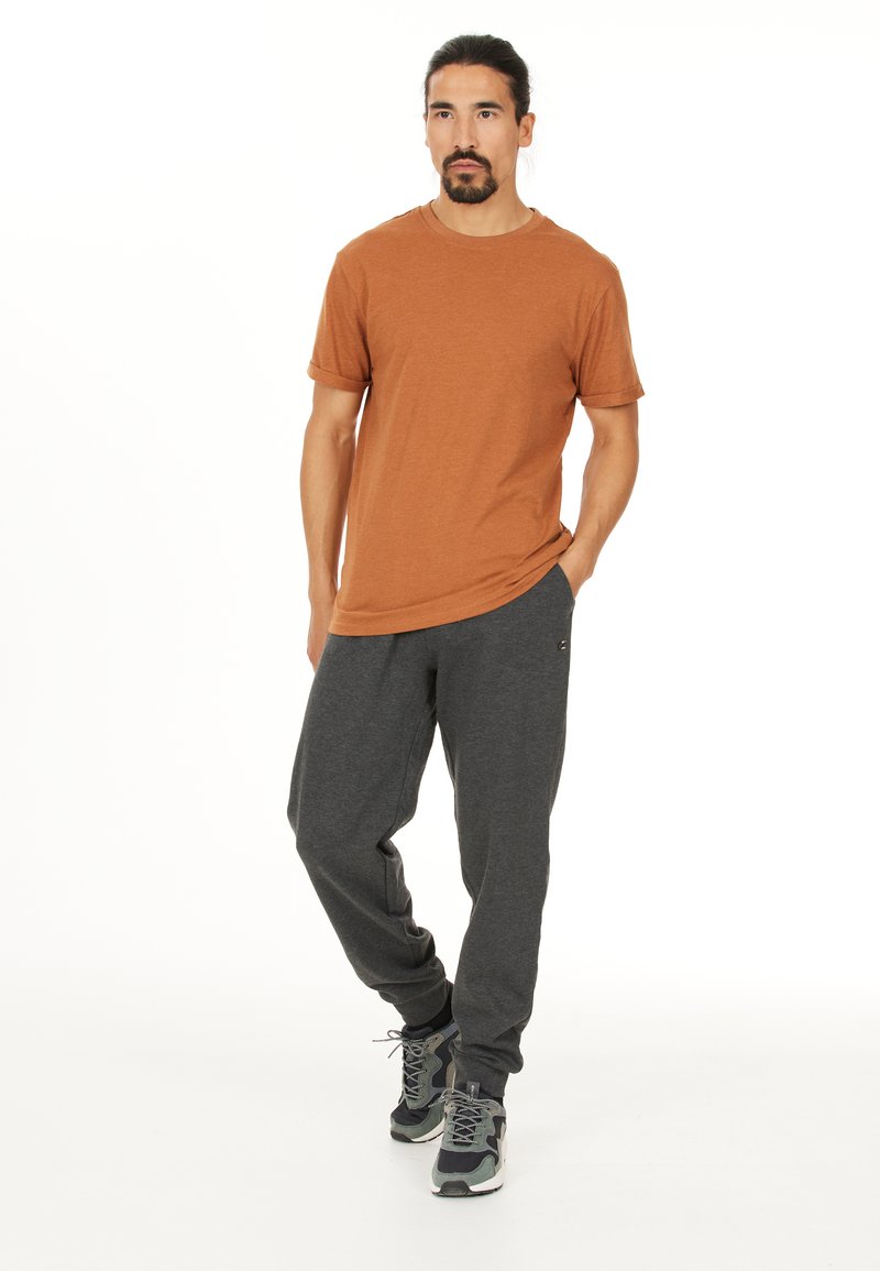 Orange kortärmad t-shirt i kombination med mörkgråa sweatpants och grå sneakers. Tyget verkar mjukt med en avslappnad passform.