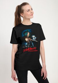 Černé bavlněné tričko s grafickým potiskem hororové postavy se drápy, obklopené temnými, děsivými barvami a textem "Noční můra v Elm Street."