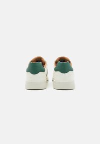 Sneakers bianchi con accenti verdi e un tallone posteriore testurizzato, caratterizzati da una fodera interna beige e una suola nera, design in pelle liscia.