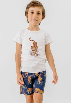Young boy wearing a white t-shirt with a walking tiger print and blue shorts patterned with tigers and leopards on a white background.