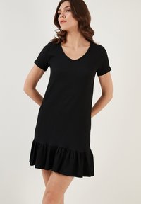 Black short-sleeve dress with a V-neckline, featuring a textured fabric and a ruffled hemline. Simple, straight-cut design.
