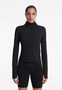 Giacca sportiva nera con colletto alto, zip completa sul davanti, maniche lunghe e tessuto elasticizzato; progettata per il comfort e la flessibilità nei movimenti.