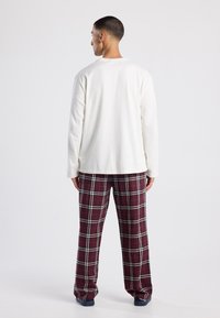 Witte lange mouwen top met ronde hals, gecombineerd met bordeauxrode geruite flanellen broek met witte accenten. Beide items hebben een relaxte pasvorm.