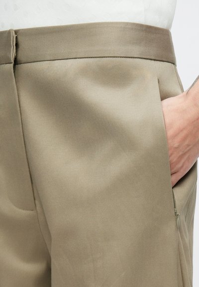 Béžové nohavice s hladkým textúrou látky, plochým predným dielom, bočným vreckom a jemným leskom, zdôrazňujúcim strihaný dizajn.