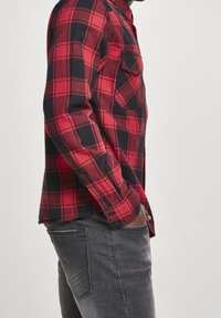 Röd och svart rutig flanellskjorta med långa ärmar, knappade manschetter och två bröstfickor, kombinerad med grå slim-fit jeans.