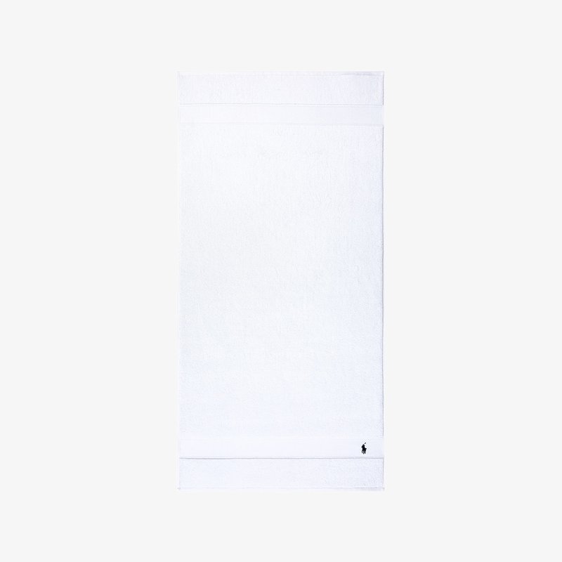 Άσπρη βαμβακερή πετσέτα μπάνιου με υφή από βρόχους, με δύο οριζόντιες ρίγες και μικρό κεντημένο λογότυπο κοντά στην κάτω γωνία.