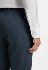 Wit overhemd met lange mouwen en knoopmanchetten, gecombineerd met donkerblauwe broek met een gestructureerde stof en een achterzakdetail.