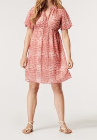 Röd- och vitmönstrad klänning med korta ärmar, markerad midja och knälång design. Matchas med ljusa remsandaler.