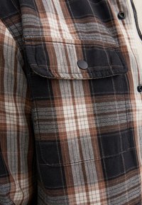 Geruite shirt in zwart, bruin en witte tinten. Gemaakt van geweven stof, met een borstzak, knoopsluiting en contrasterende texturen.