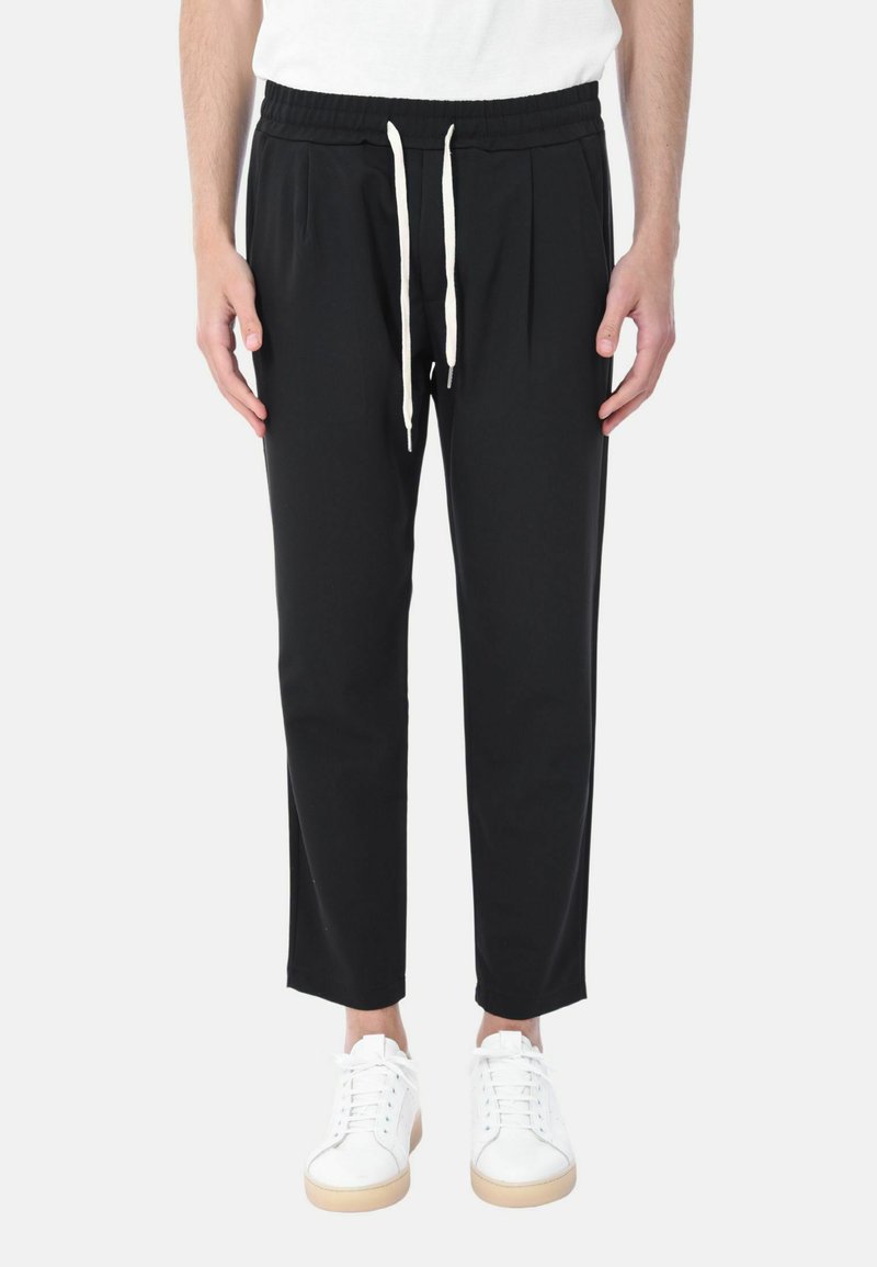Pantaloni neri a sigaretta con vita elastica e coulisse, caratterizzati da pieghe sulla parte anteriore, abbinati a sneakers bianche.