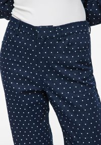 Granatowe spodnie w groszki wykonane z denimu z jasnoniebieskimi kropkami, wyposażone w pas z szlufkami na pasek oraz boczne kieszenie.
