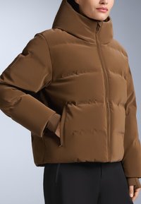 Smeđi podstavljeni kaput s visokim ovratnikom, s prednjim patentnim zatvaračem i skrivenim bočnim džepovima. Materijal ima glatku, sjajnu teksturu.