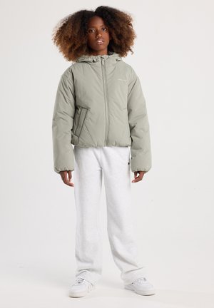 Een lichtgroene pufferjack met een ritssluiting aan de voorkant, een capuchon en zijzakken. Gekocht met lichtgrijze joggingbroeken en witte sneakers.
