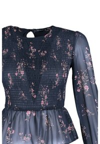 Marineblå peplumtop med blomsterprint, smocket liv, lange gennemsigtige ærmer og detalje med nøglehul bagpå. Fremstillet af letvægtsstof.