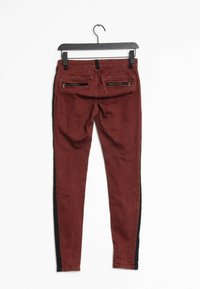 Pantalons skinny bordeaux avec des panneaux latéraux noirs, dotés de deux poches arrière zippées et d'une texture lisse. Accrochés à un crochet noir.