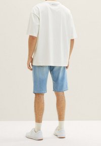 Camiseta blanca de gran tamaño con mangas cortas, combinada con pantalones cortos de mezclilla azul claro. Zapatillas blancas y calcetines tipo crew completan el atuendo.