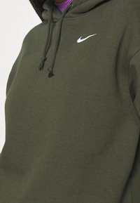 Oliwkowy kaptur z teksturowanym wykończeniem, z białym logo Nike na piersi i sznurkami do kaptura.